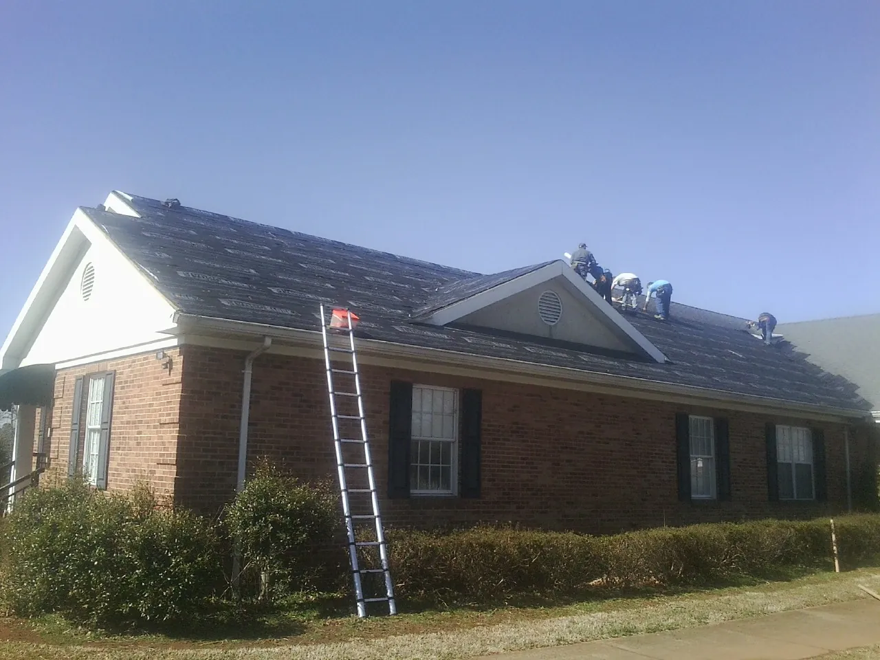 Crew tearing shingles off a brick ranch roof with a ladder set — Metal Roof Repair work by our crew in Thousand Palms