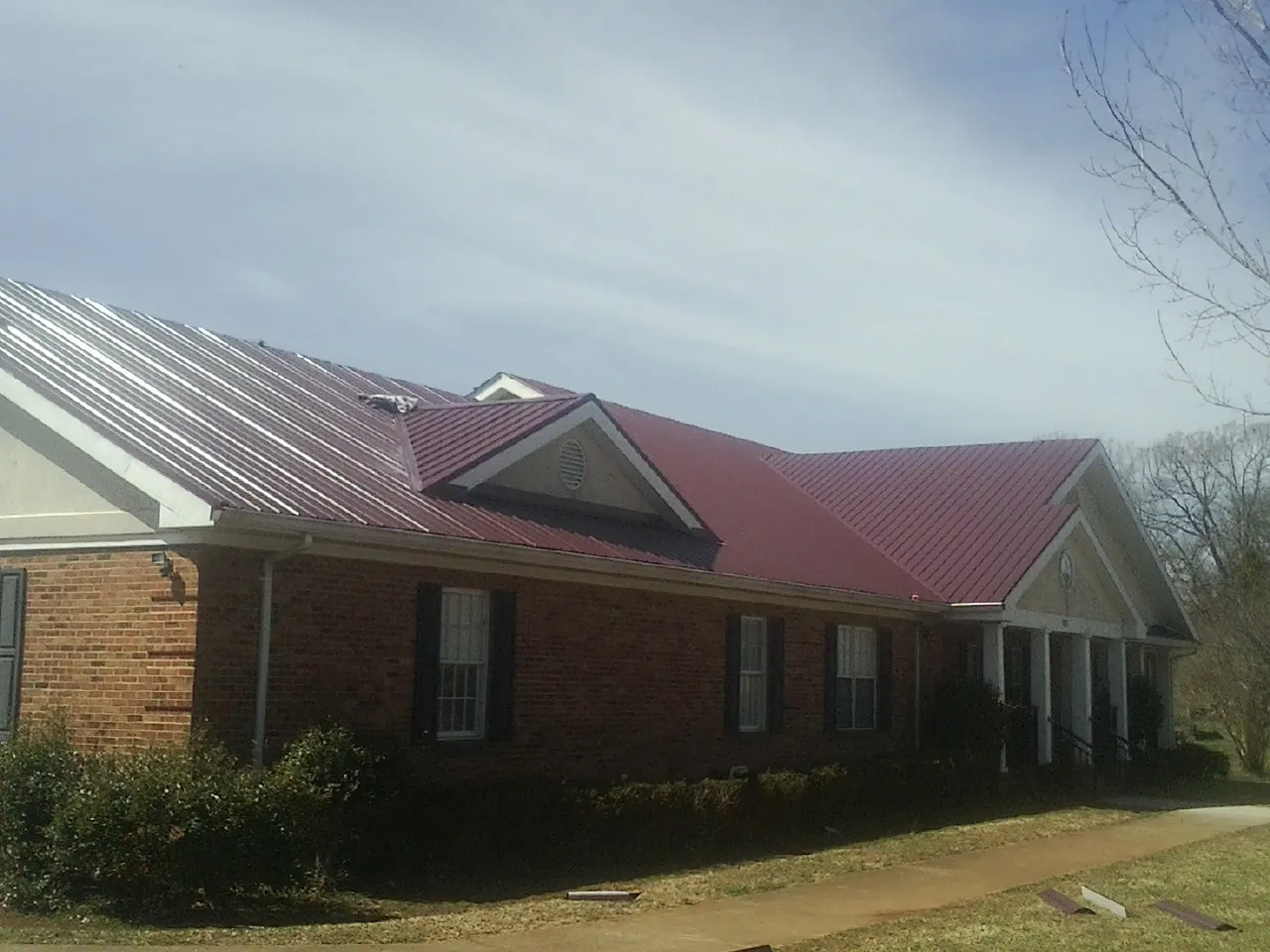 Red metal roof with gabled entries on a long brick building, from a Hail Damage Roof Repair job in Thousand Palms