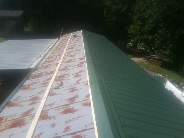 Old rusted panels beside newly installed green metal roofing — Wind Damage Roof Repair by Roofing Brothers in Thousand Palms
