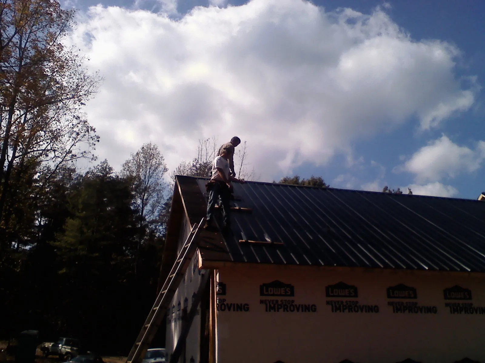 Roofer fastening dark metal panels high against a cloudy sky, from a Roof Inspection job in Thousand Palms