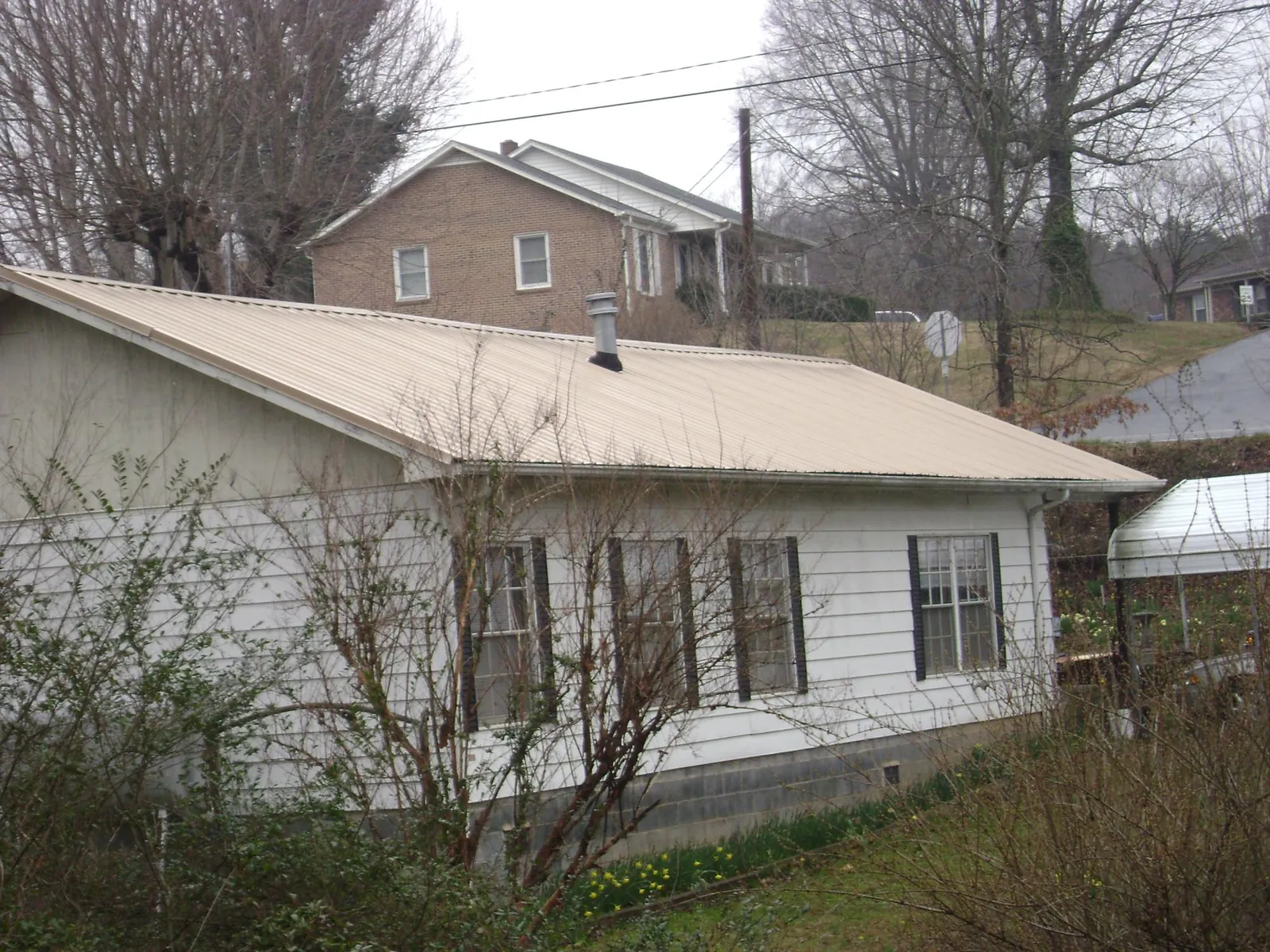 Tan metal roof on a white sided house set into a hillside — Commercial Roofing by Roofing Brothers in Thousand Palms